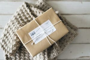 subscription box in brown paper with delivery label tied with string on knitted scarf