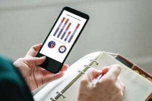 person writing in productivity journal while looking at time tracking report on smartphone