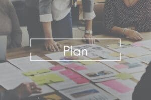 people leaning over a table covered in papers - a business continuity plan