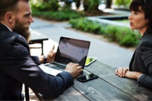 two people doing remote work at picnic table outside with computers