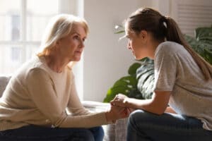 Grown up daughter holding hands of middle aged mother relatives female sitting look at each other having heart-to-heart talk about downsizing