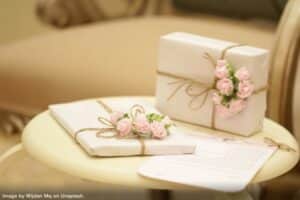 two small clutter-free wedding gifts wrapped in white paper with small pink roses attached with a bow