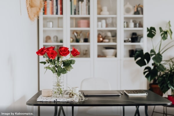 red roses and laptop on tidy desk in front of beautifully organized cupboards representing the cost of decluttering and organizing