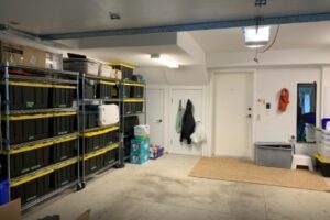 looking at the left hand side of the organized garage using black bins with yellow lids on stainless steel shelving pushed up to the wall with no clutter on the floor