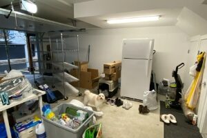 looking at the left hand side of an untidy garage with clutter on the floor and refrigerator in the middle of the wall