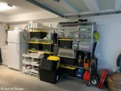 looking at the right hand side of the organized garage with the freezer and fridge neatly against the wall beside stainless steel shelving holding bins of various sizes