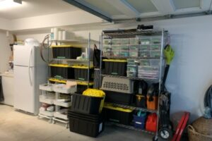 looking at the right hand side of the organized garage with the freezer and fridge neatly against the wall beside stainless steel shelving holding bins of various sizes