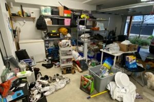 looking at the right hand side of an untidy garage with clutter on the floor and a freezer and shelving against one wall and shelves in the middle of the floor